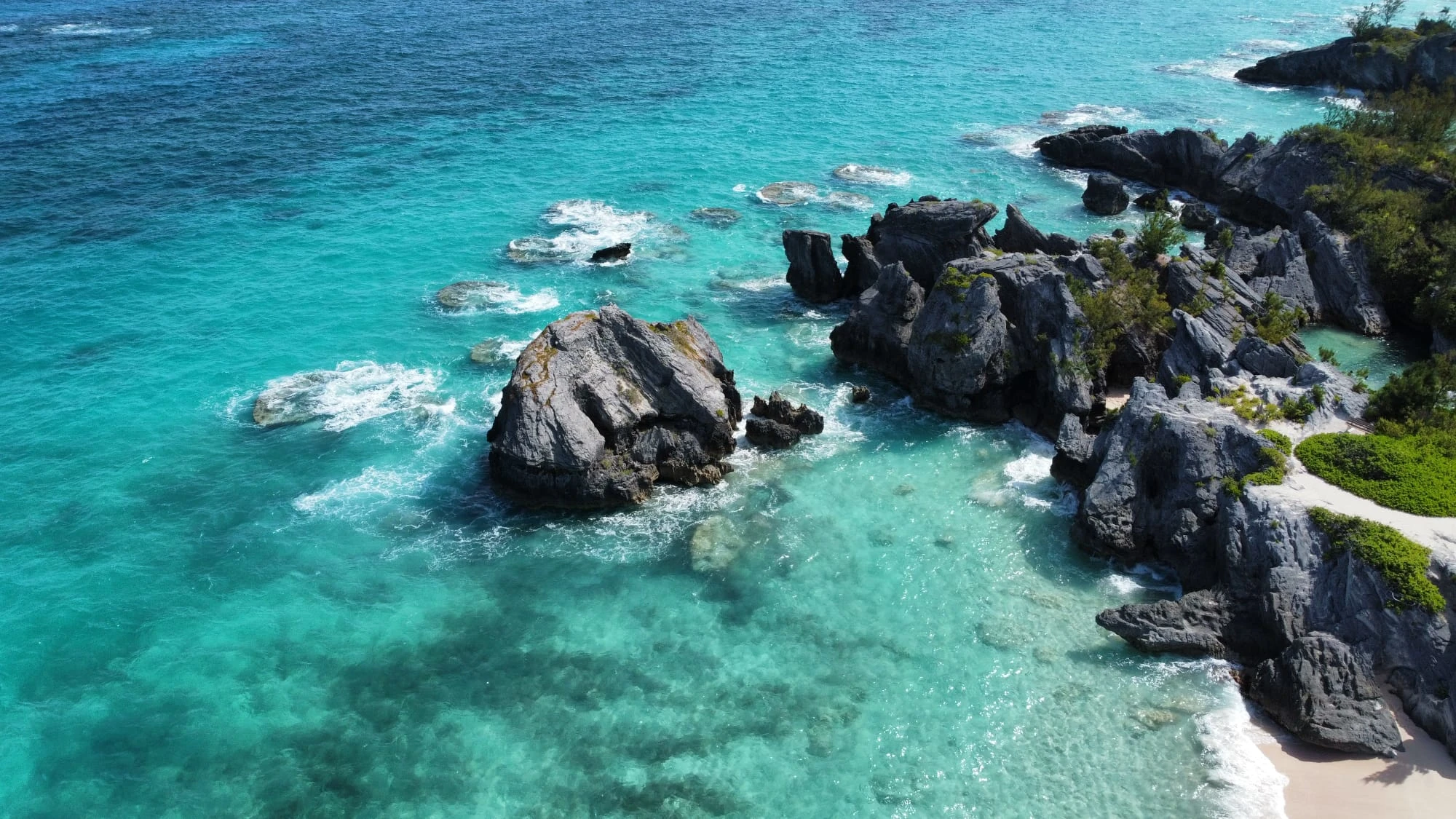 Aerial image of whiteish-pink beaches, clear blue water, and grey rocky outcrops